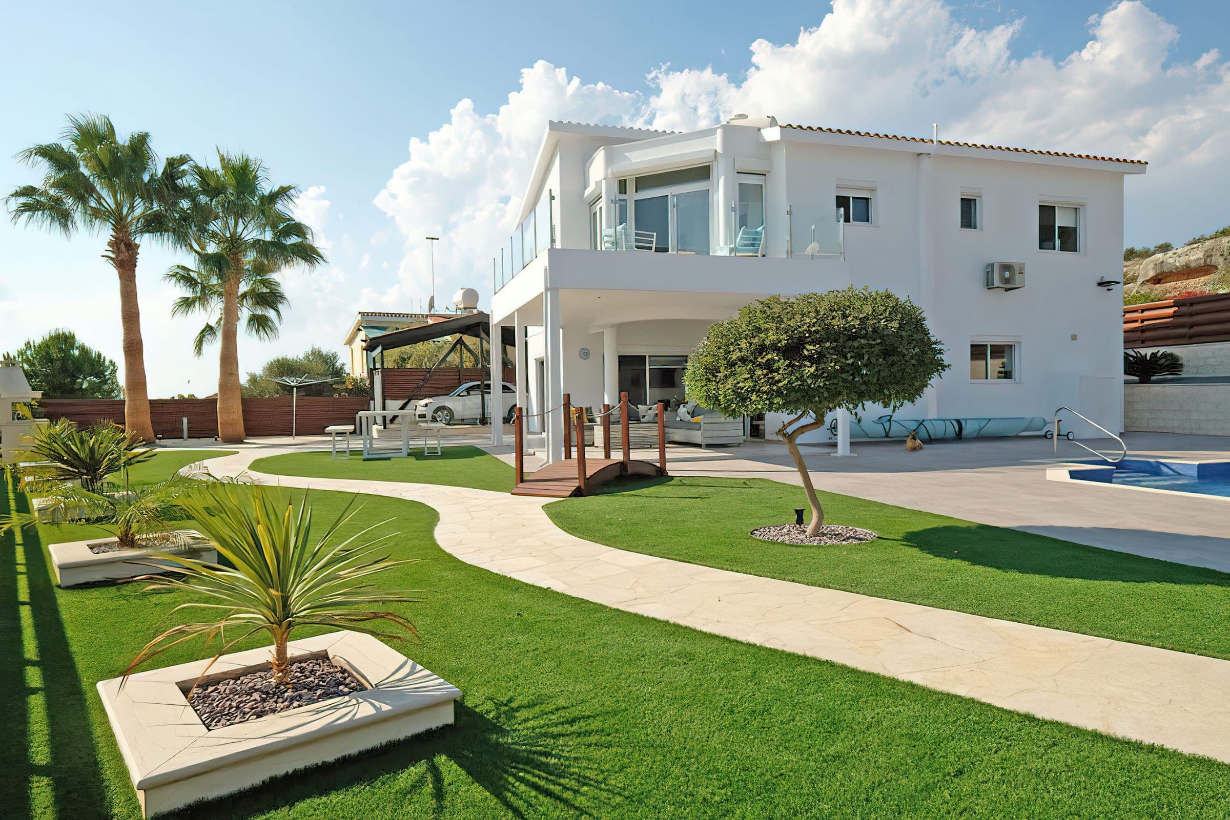 Landscaped garden with lawn, palm trees and a wooden bridge in front of the villa