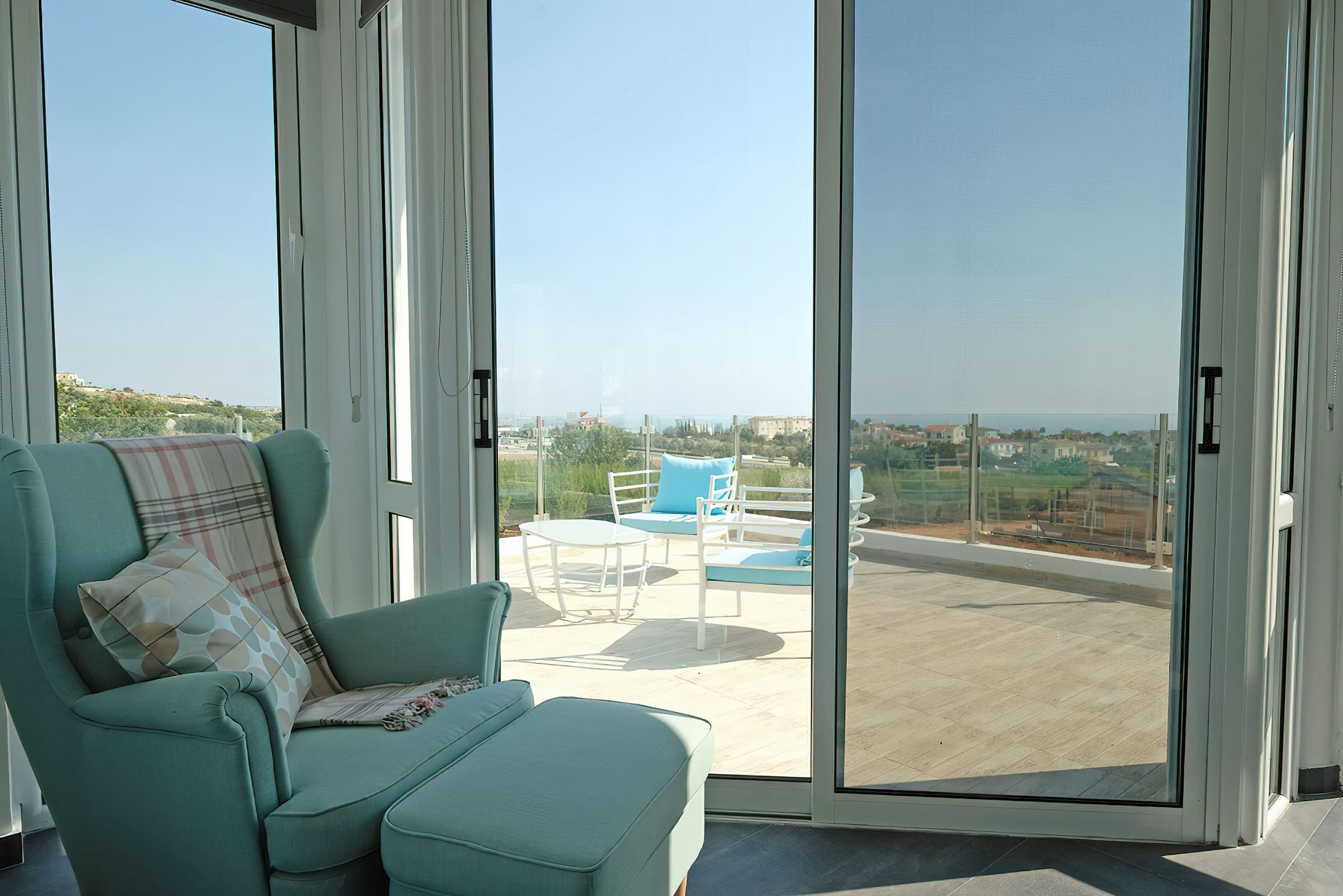 Armchair by the master bedroom's glass doors opening onto a balcony with sea and country views