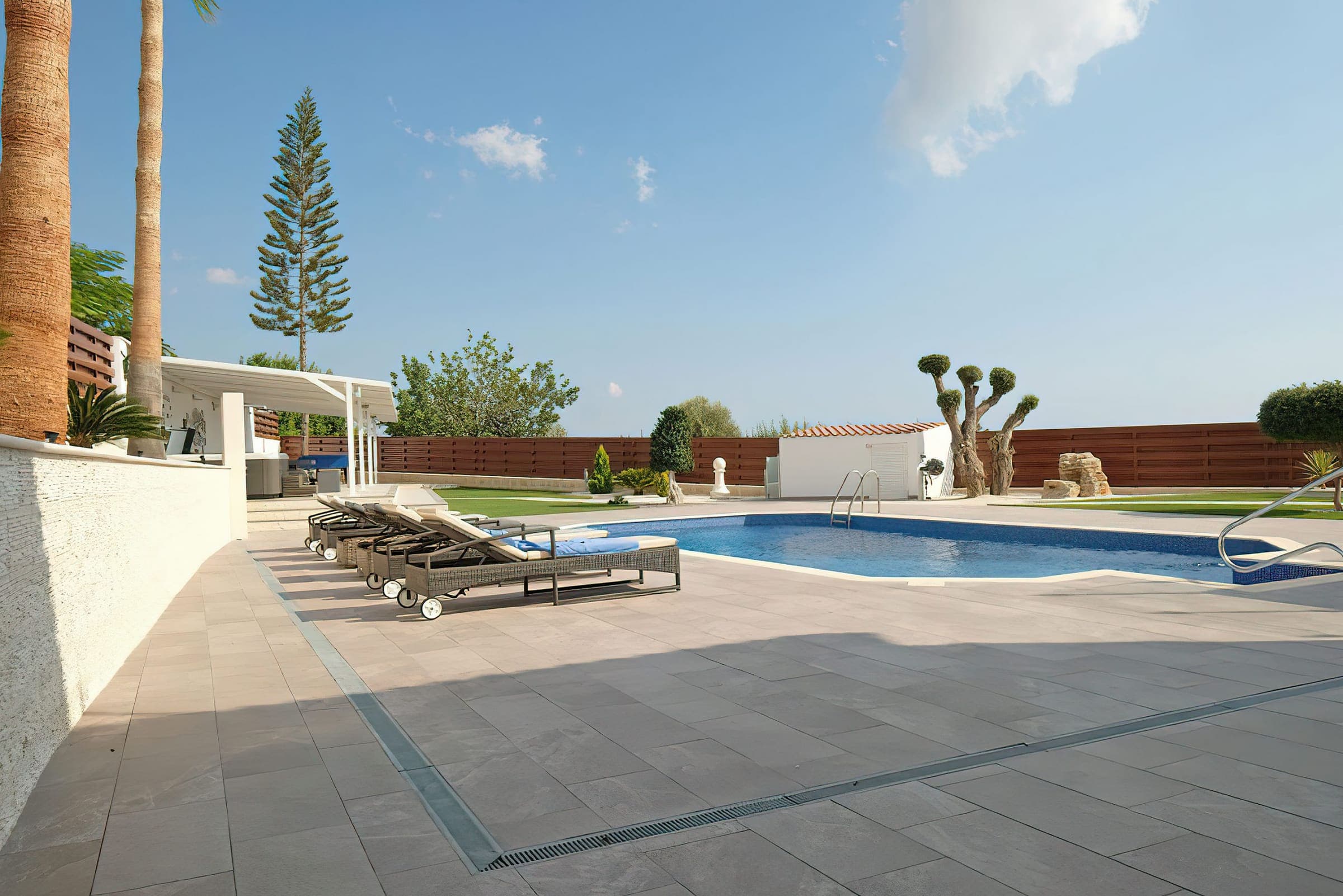 Pool terrace with sun loungers and olive trees under a blue sky