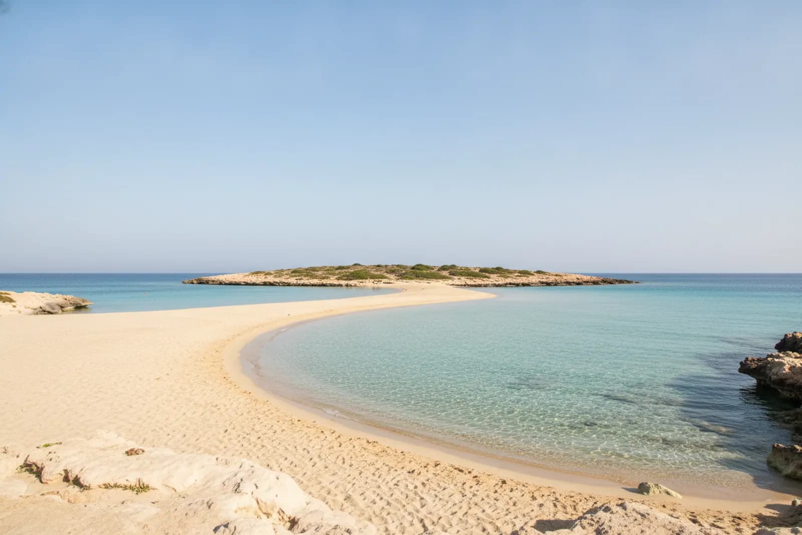 Sabbia dorata chiara e acqua bassa e turchese a Nissi Beach, vicino ad Ayia Napa, a Cipro, con un isolotto roccioso al largo