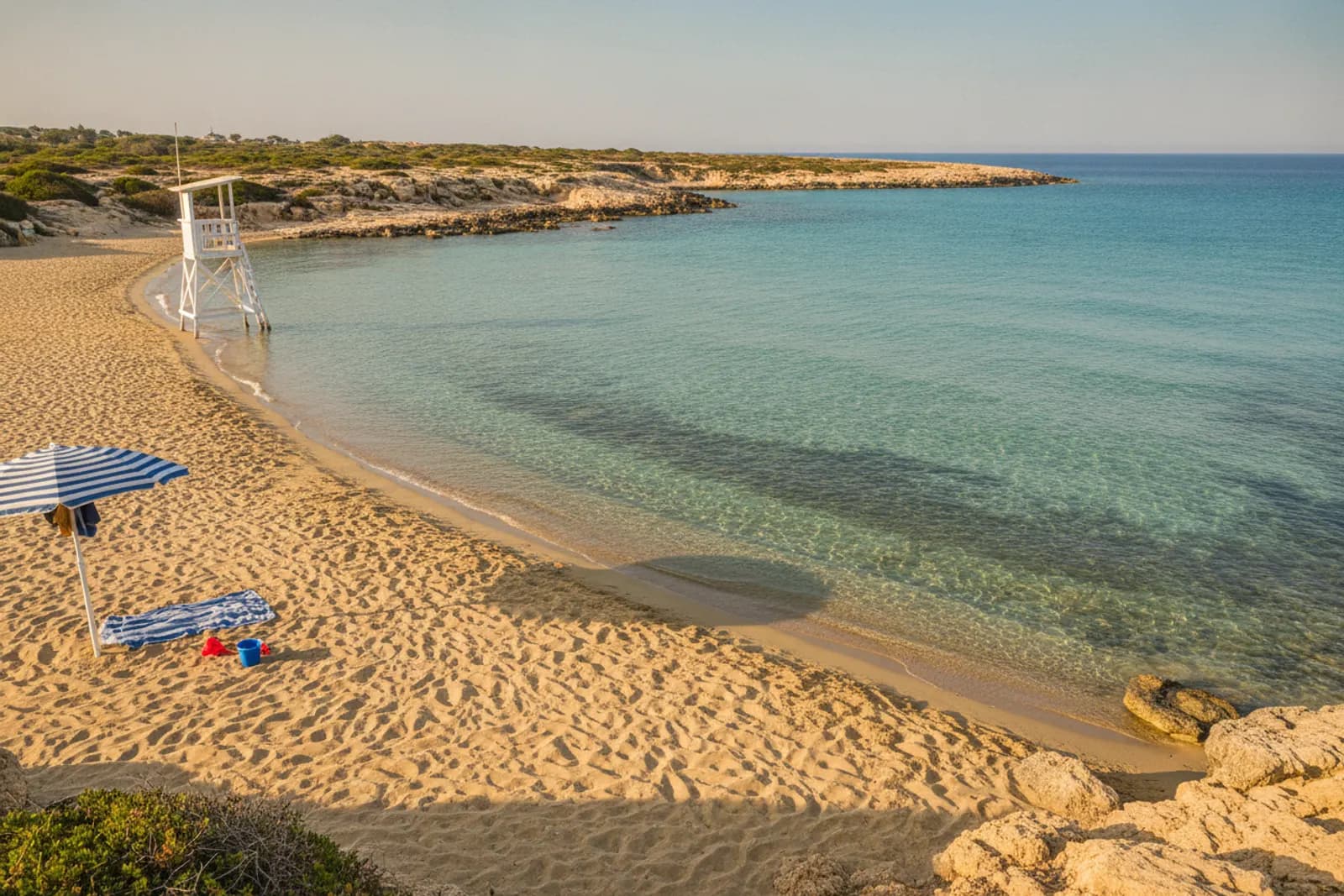 Baia sabbiosa calma e bassa, con secchiello e paletta sotto un ombrellone e una torretta dei bagnini, costa ovest di Cipro.
