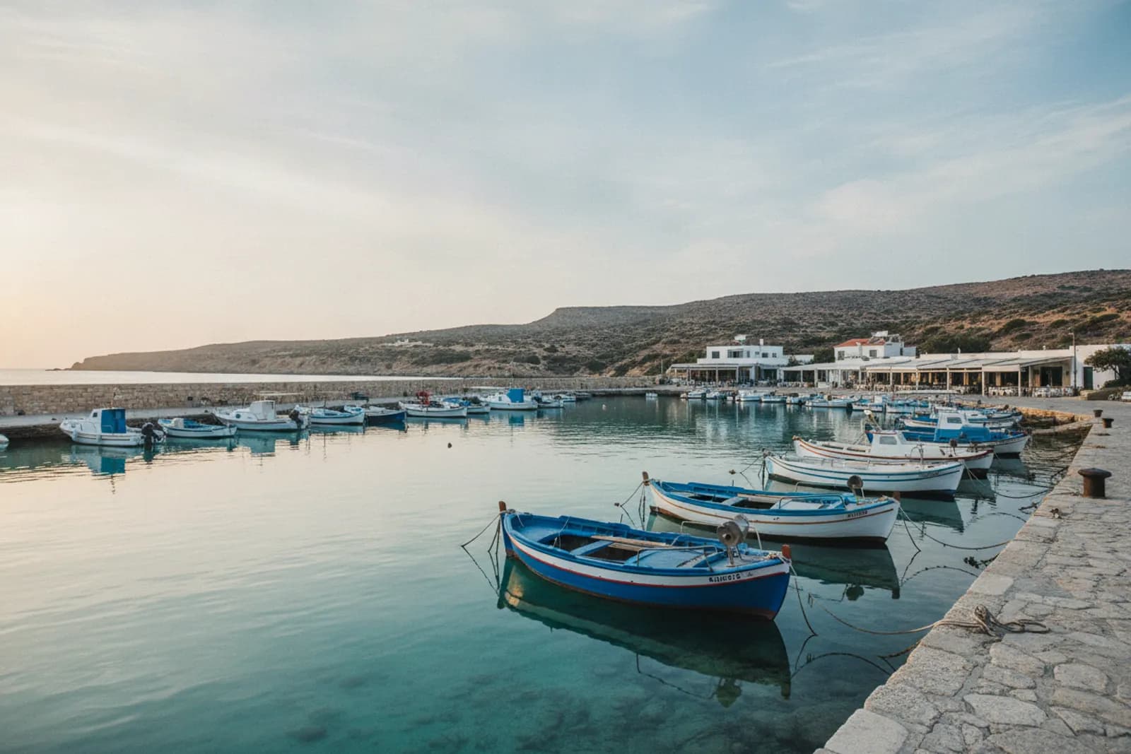 Barche da pesca ormeggiate in un porticciolo dall’acqua turchese e calma, con le colline aride dell’Akamas alle spalle