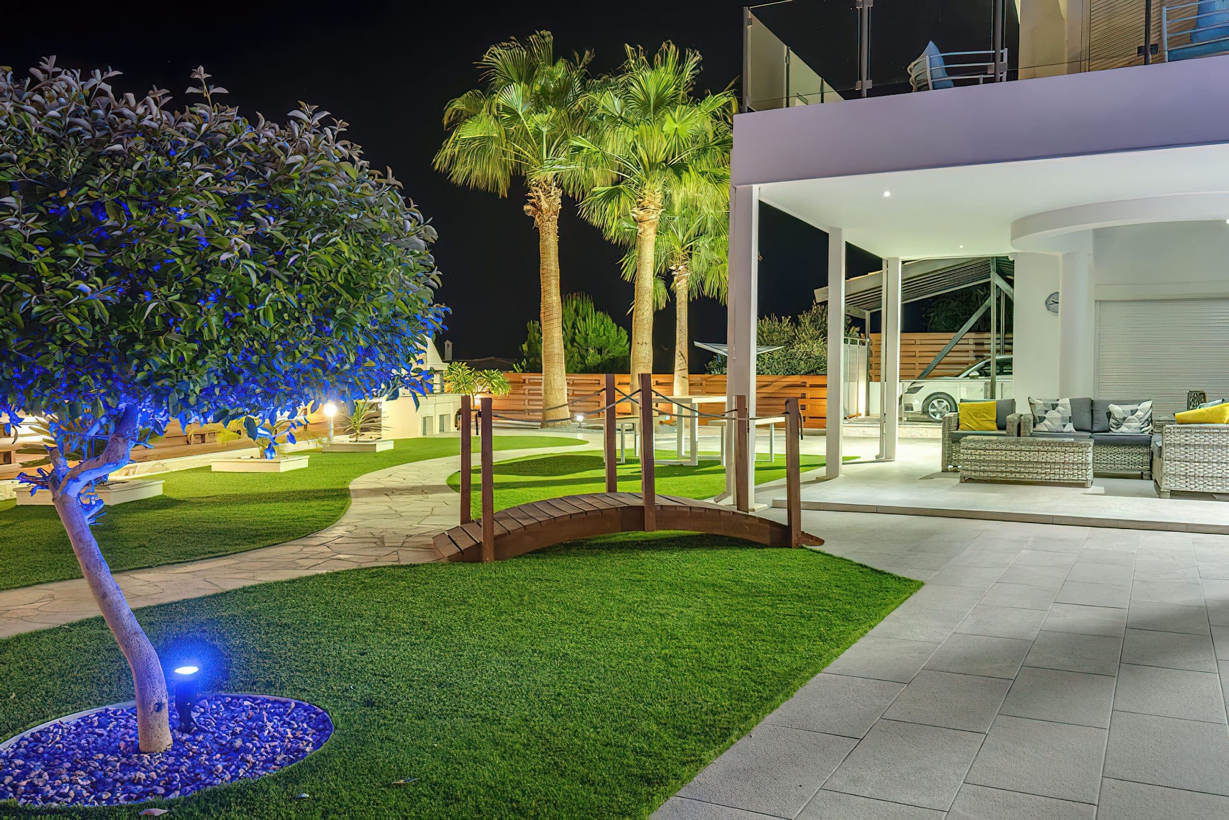 Garden at night with an illuminated olive tree and wooden bridge